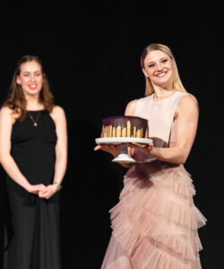Smuin artists Brandon Alexander and Brennan Wall look on as Tessa Barbour shows off her homemade chocolate cake, auctioned off at Smuin's Annual Gala in 2023.